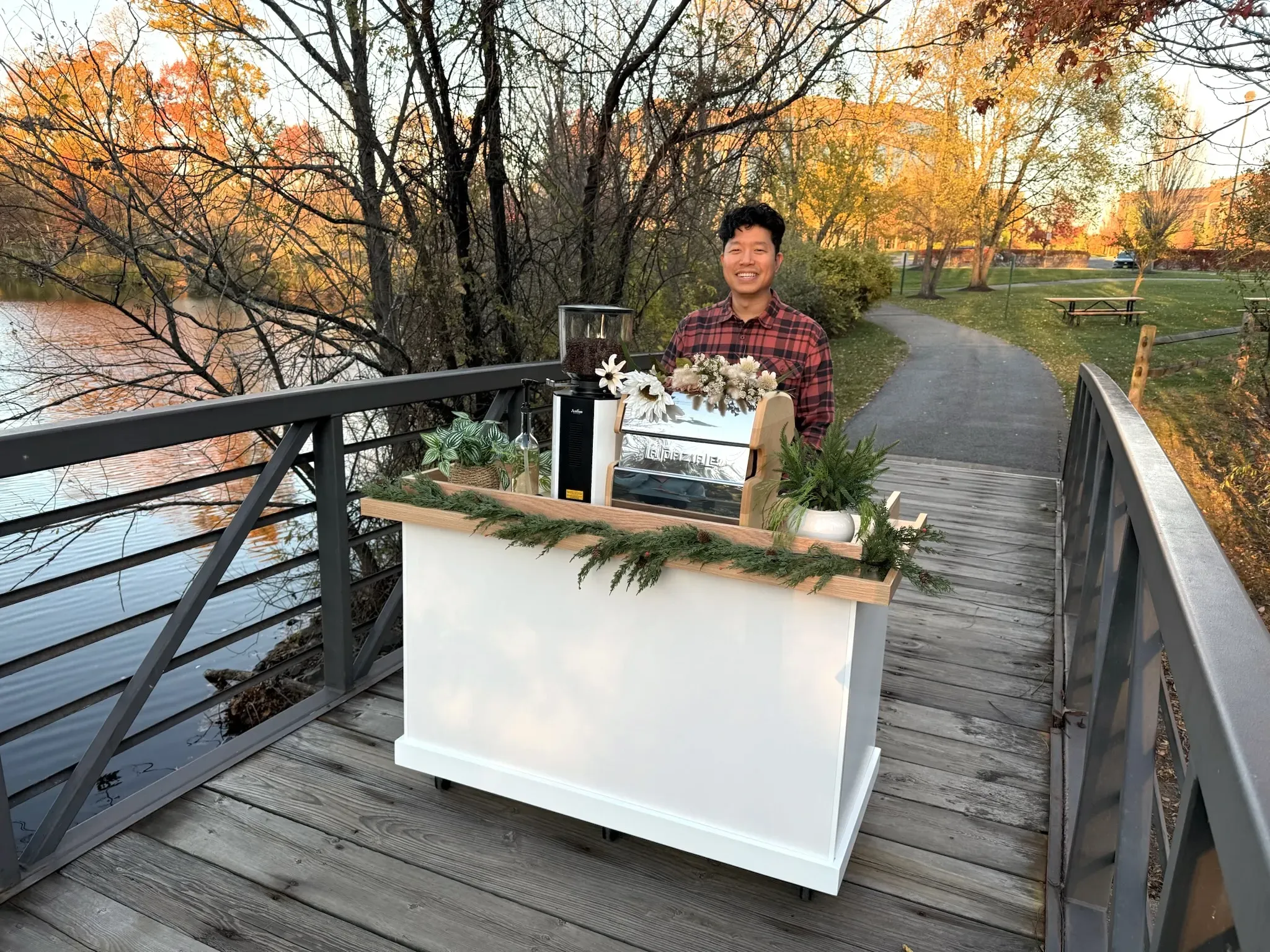 Mike Park standing behind the coffee cart on a footbridge in autumn